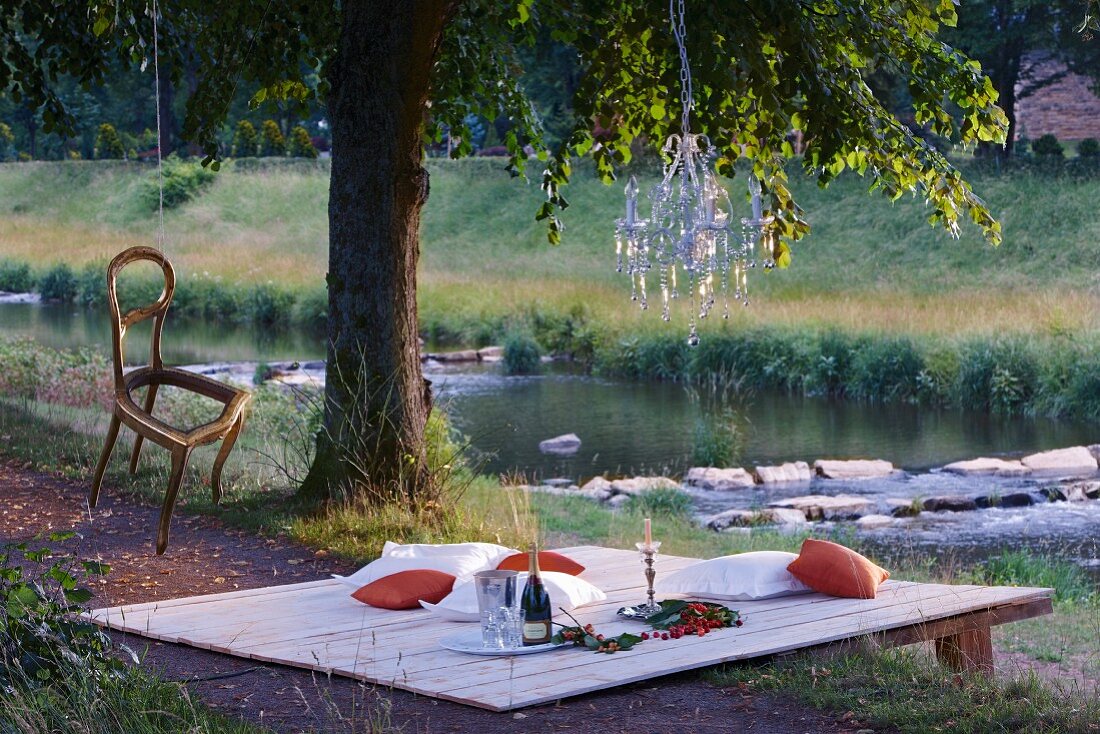 Picnic by the river decorated with chandelier and chair hung from tree