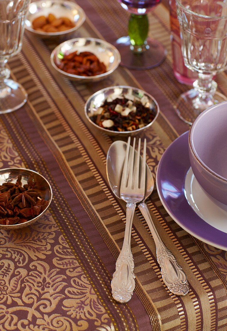 Elegant gedeckter Tisch mit violett-goldfarbener Tischdecke, Silberbesteck und Silberschälchen