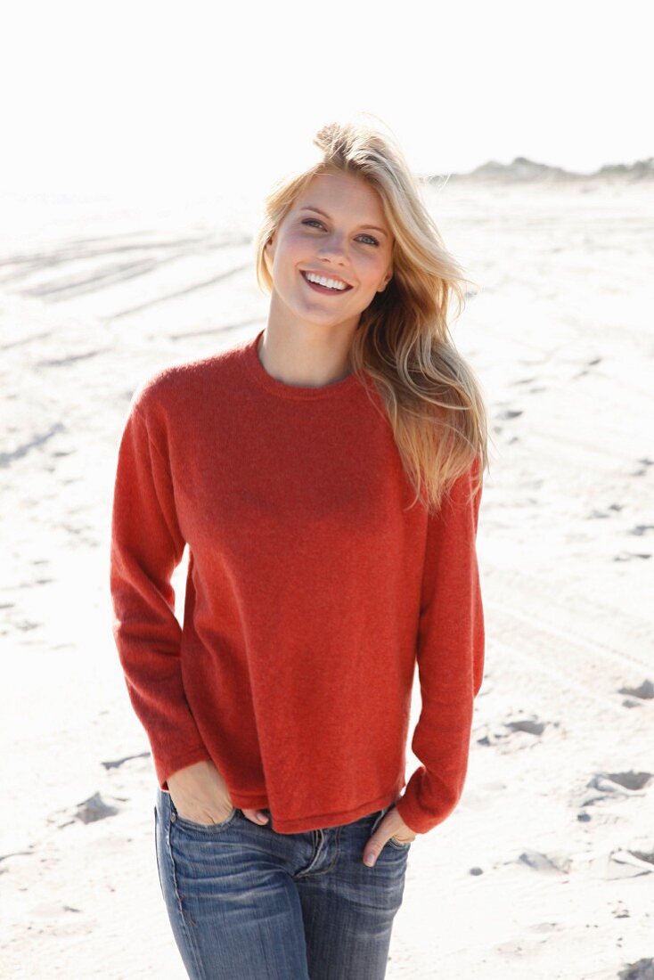 Junge Frau in rostrotem Pulli und Jeans am Strand