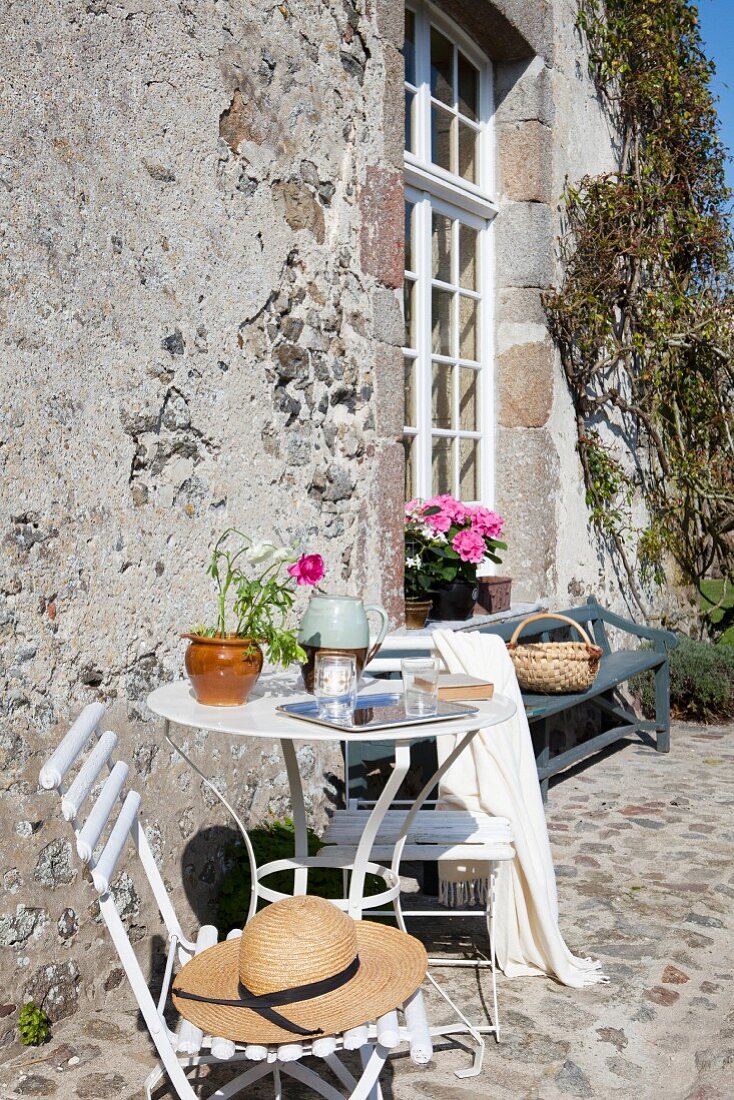 Sunny seating area outside rustic country house with garden bench and lattice window in background