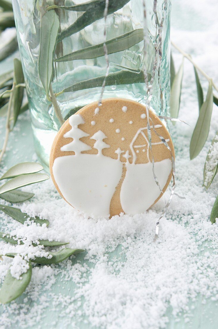 About biscuits iced with a winter landscape between olive sprigs on a table covered with snow
