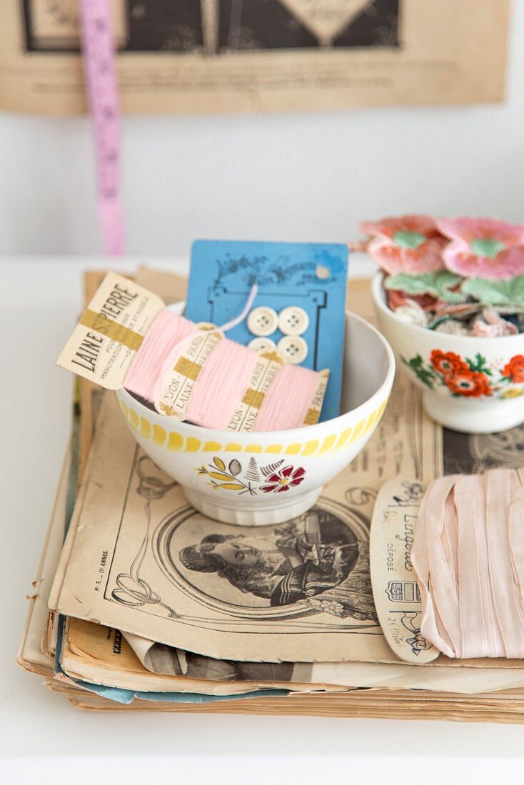 Old sewing utensils in bowl with floral motif on stack of papers