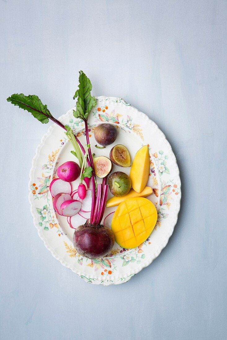 Fresh radishes, beetroot, mango and figs on a plate (seen from above)