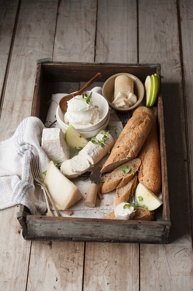 Various types of cheese and a baguette on a wooden tray