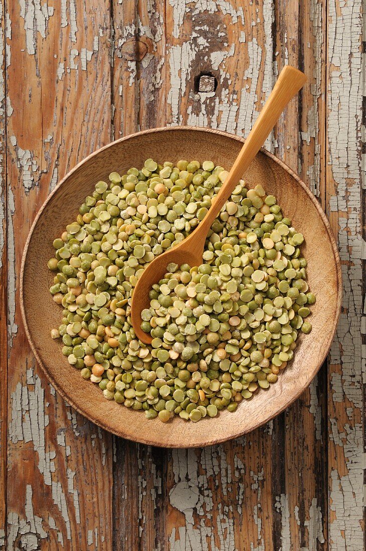 Split peas in a wooden bowl with a wooden spoon (seen from above)