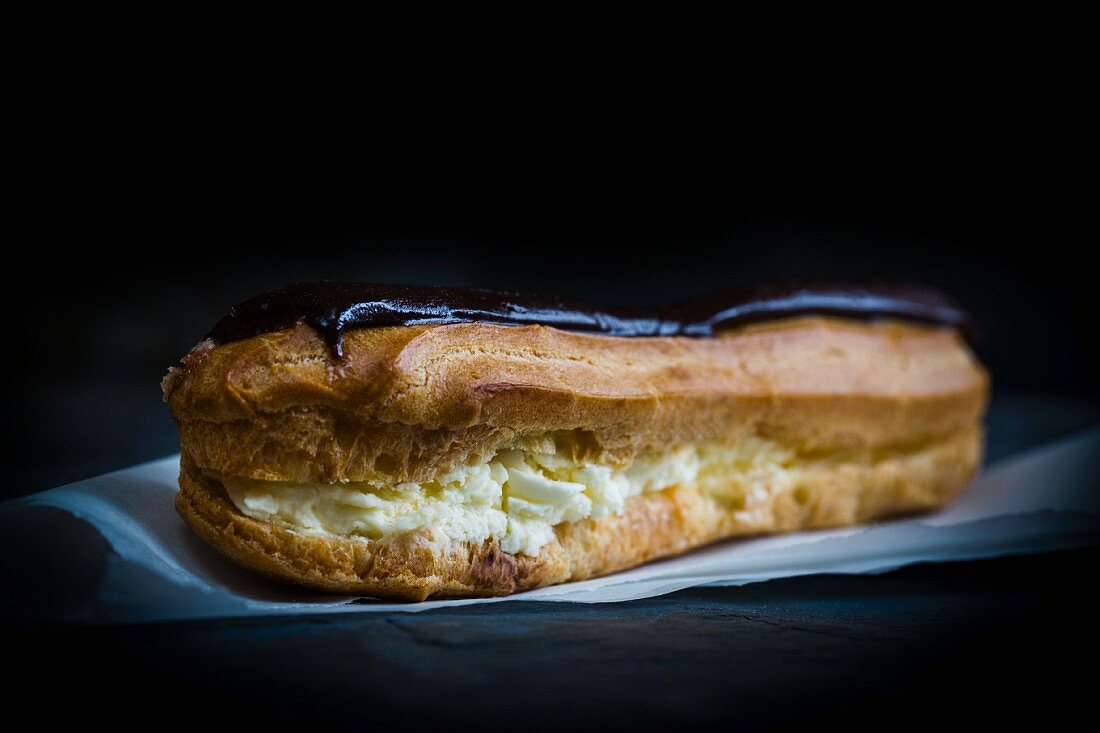 A chocolate eclair filled with cream and topped with chocolate glaze