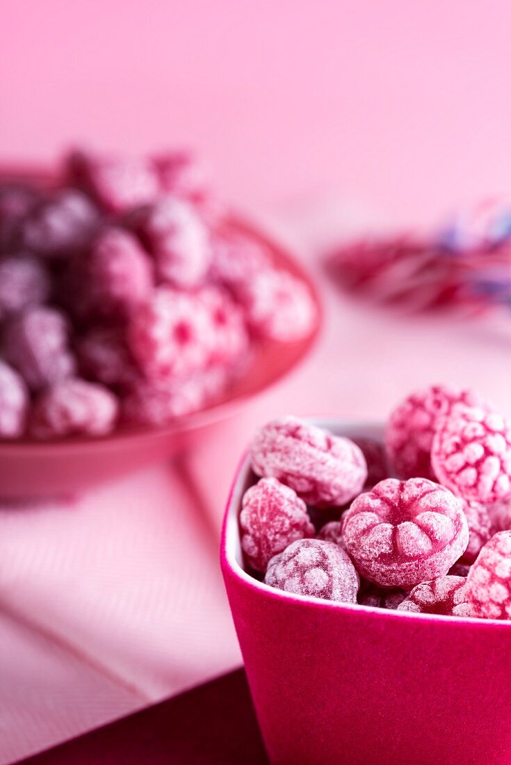 Raspberry sweets in pink bowls on a pink surface