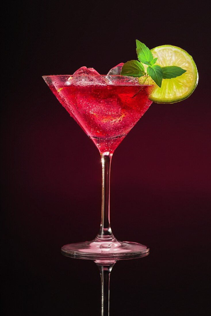 Rosa Cocktail im Glas mit Limettenscheibe und Minze auf dunklem Untergrund