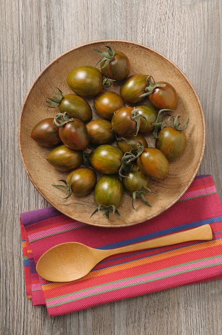 Schwarze Tomaten auf Holzteller (Aufsicht)