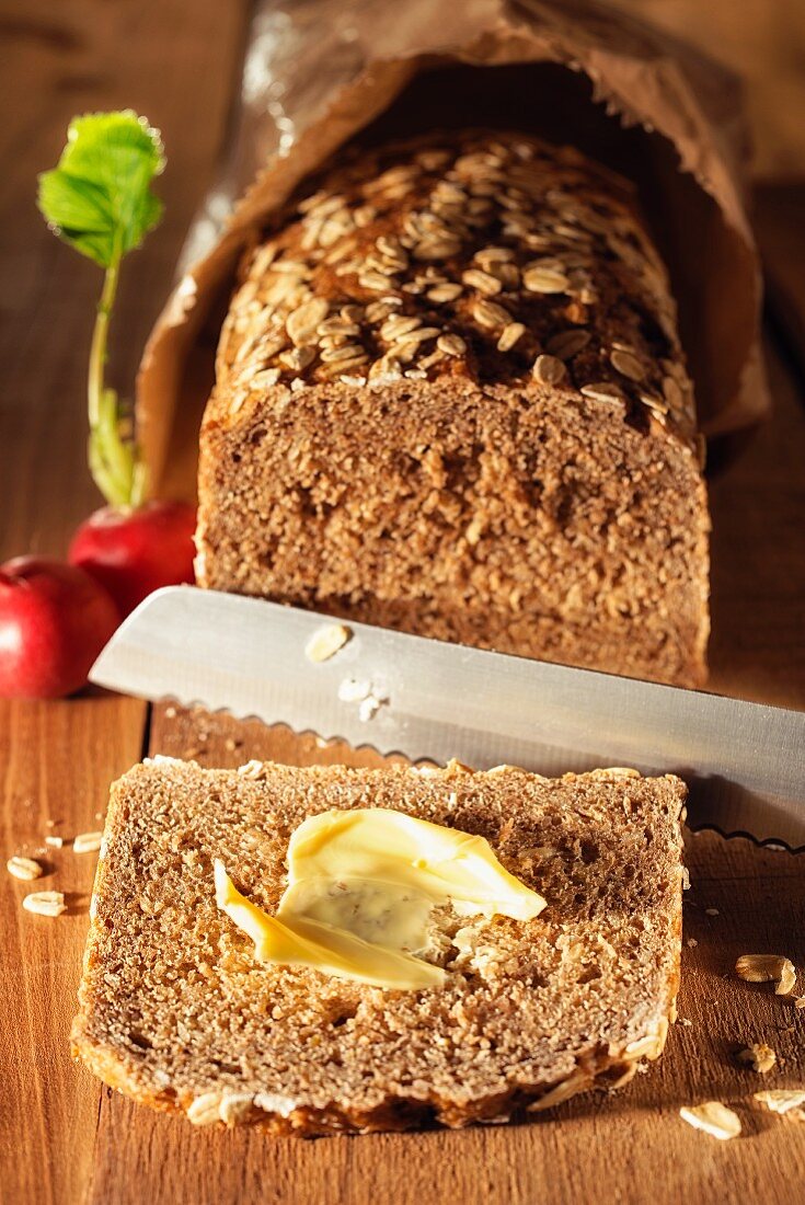 Angeschnittenes Brot mit Brotmesser und Radieschen auf Holzbrett