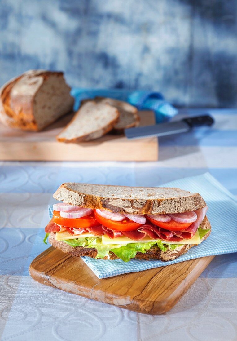Sandwich auf hellblauer Serviette auf Holzbrett vor aufgeschnittenem Brotlaib