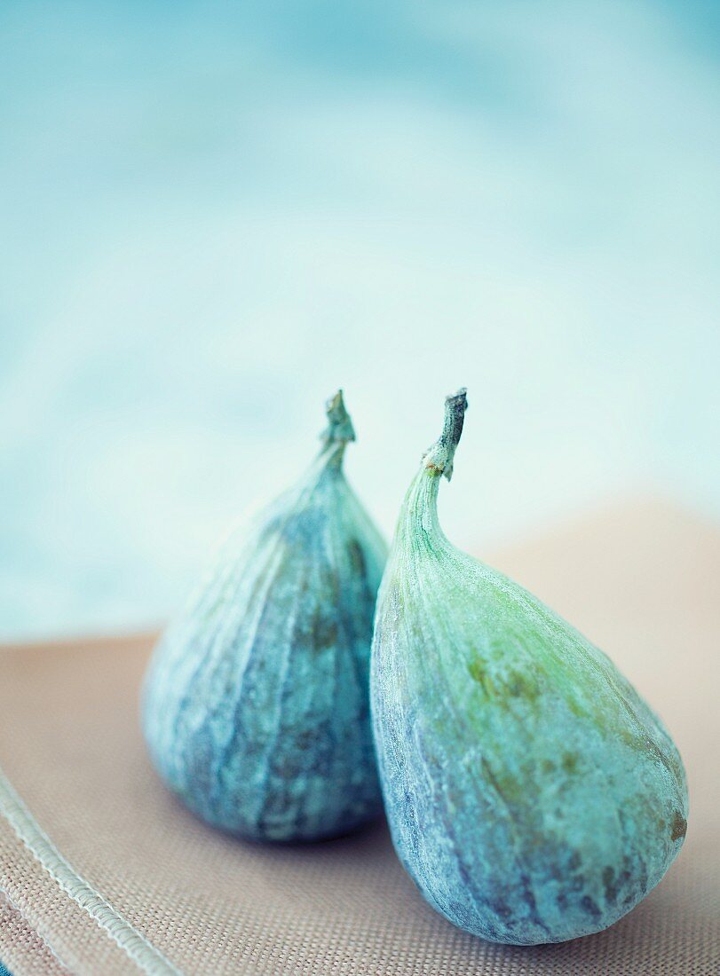 Two figs on a brown tea towel against a light blue background