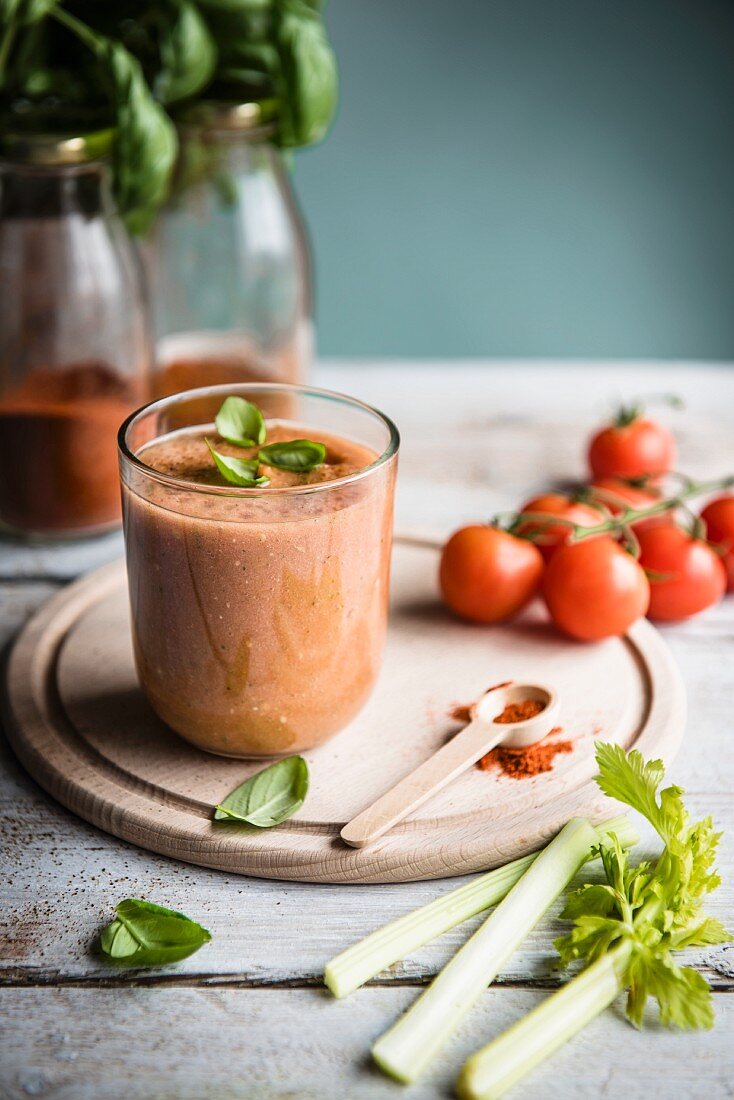 Ein Glas Tomaten-Smoothie mit frischen Basilikumblättern und Rispentomaten