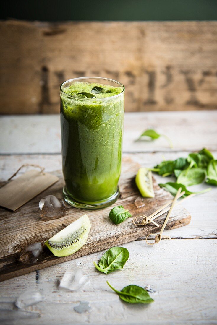 A glass of kiwi and spinach smoothie with fresh spinach leaves and slices of kiwi