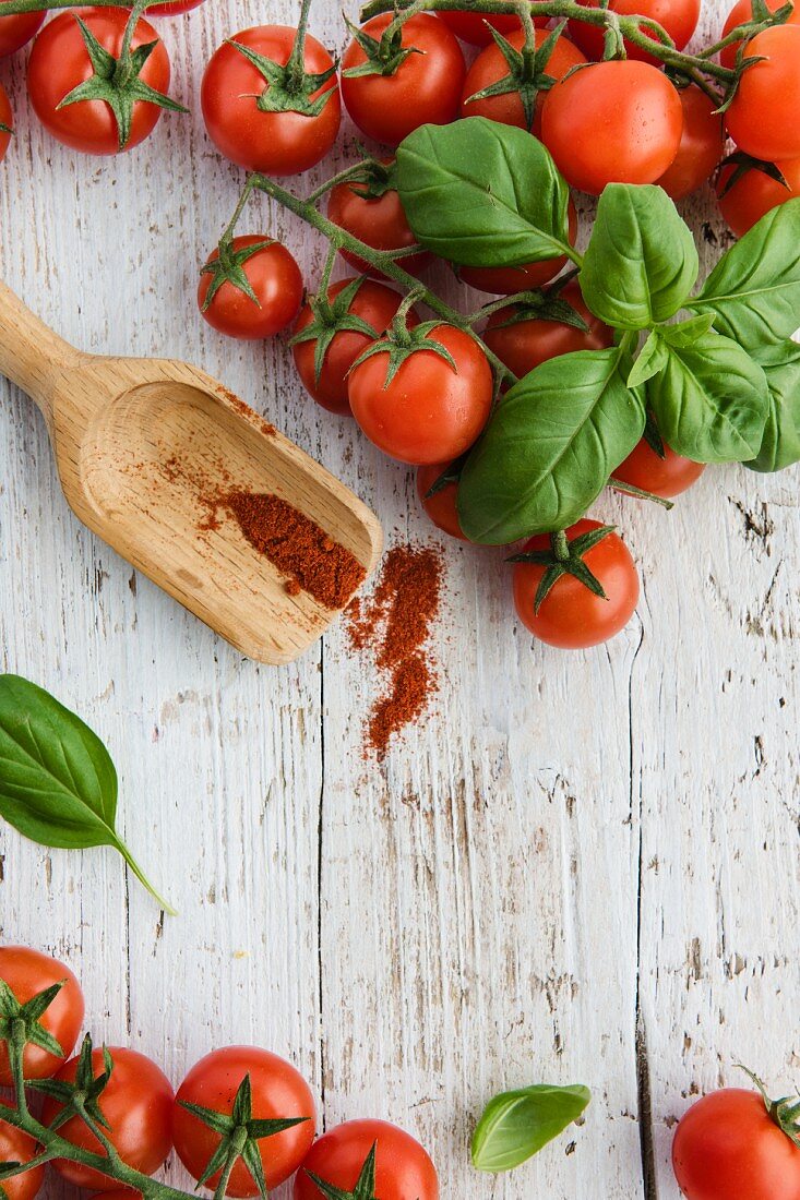 Kirschtomaten, Basilikumblätter und Cayennepfeffer auf weißem Holzbrett (Draufsicht)