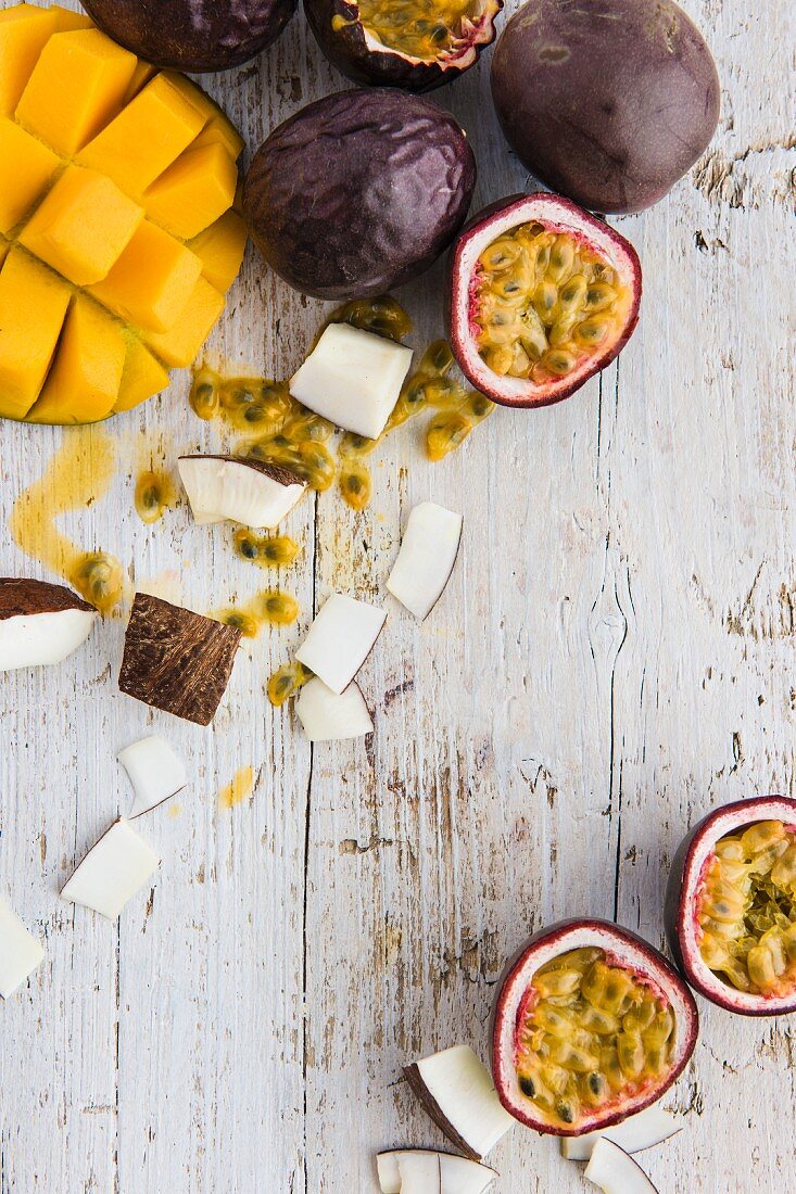 Passionsfrüchte, Kokosnussstückchen und Mango auf weißem Holzbrett (Draufsicht)