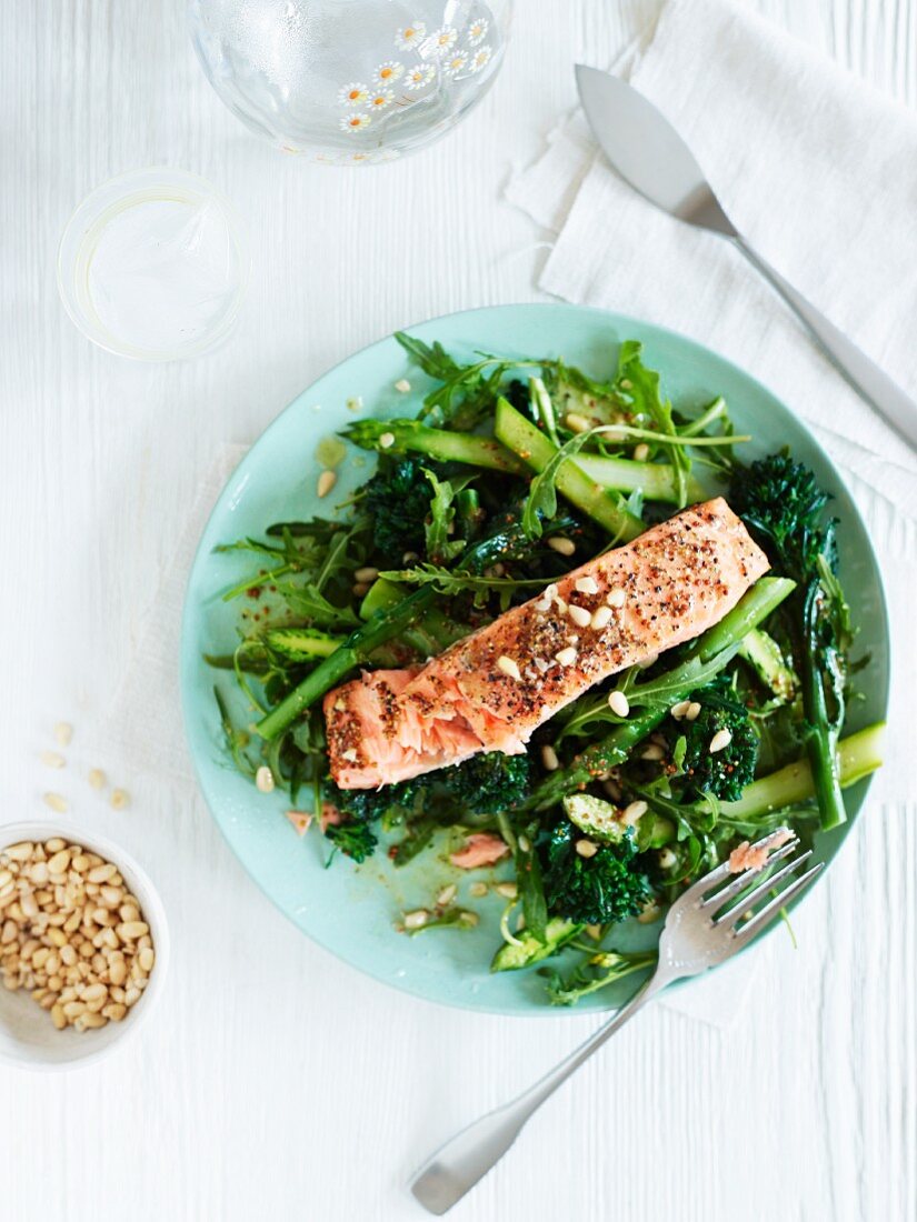 A salmon fillet on a bed of green vegetables with pine nuts