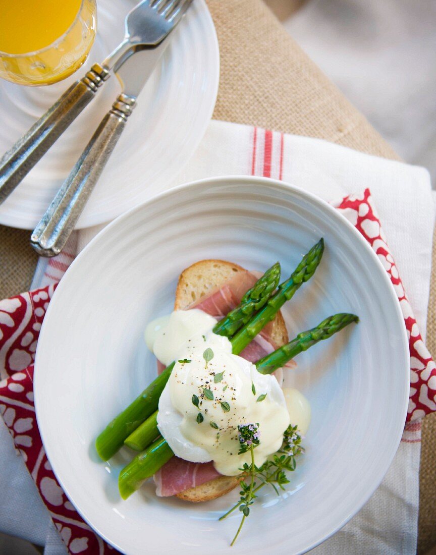 A poached egg on a slice of bread and ham with green asparagus and Hollandaise sauce