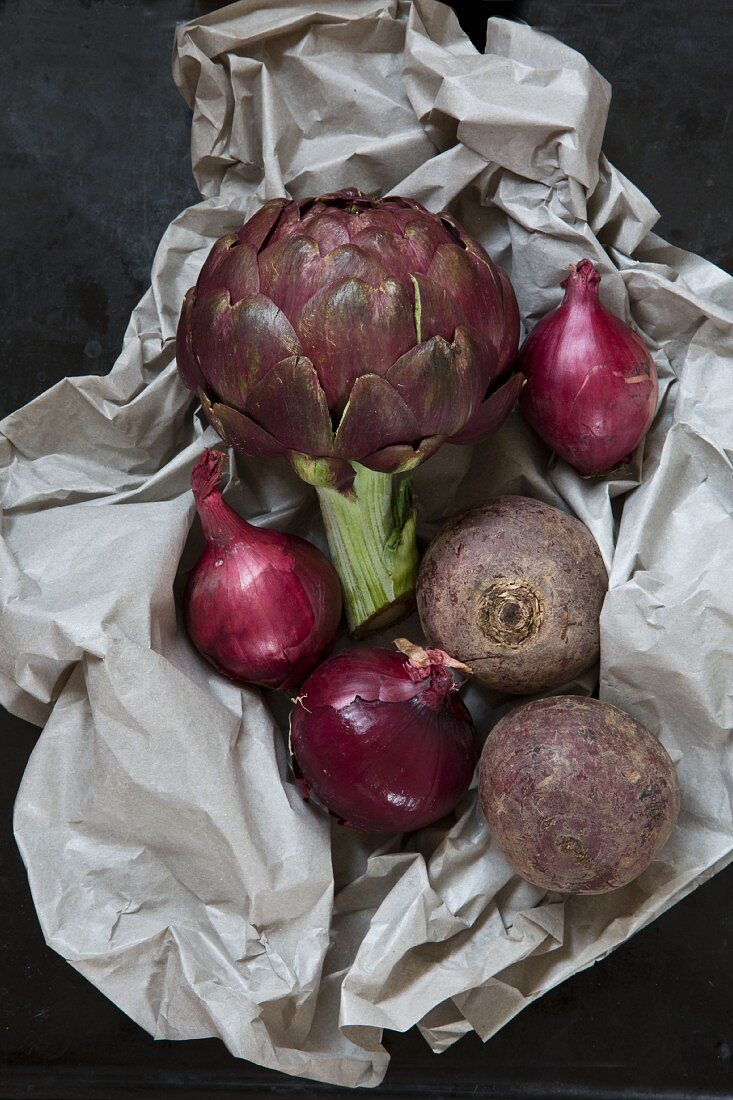 An arrangement of vegetables featuring artichoke, red onions and beetroot on piece of paper