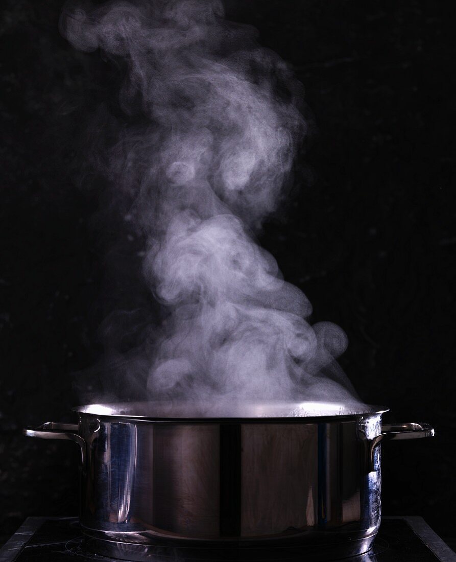 A steaming pot of water against a black background