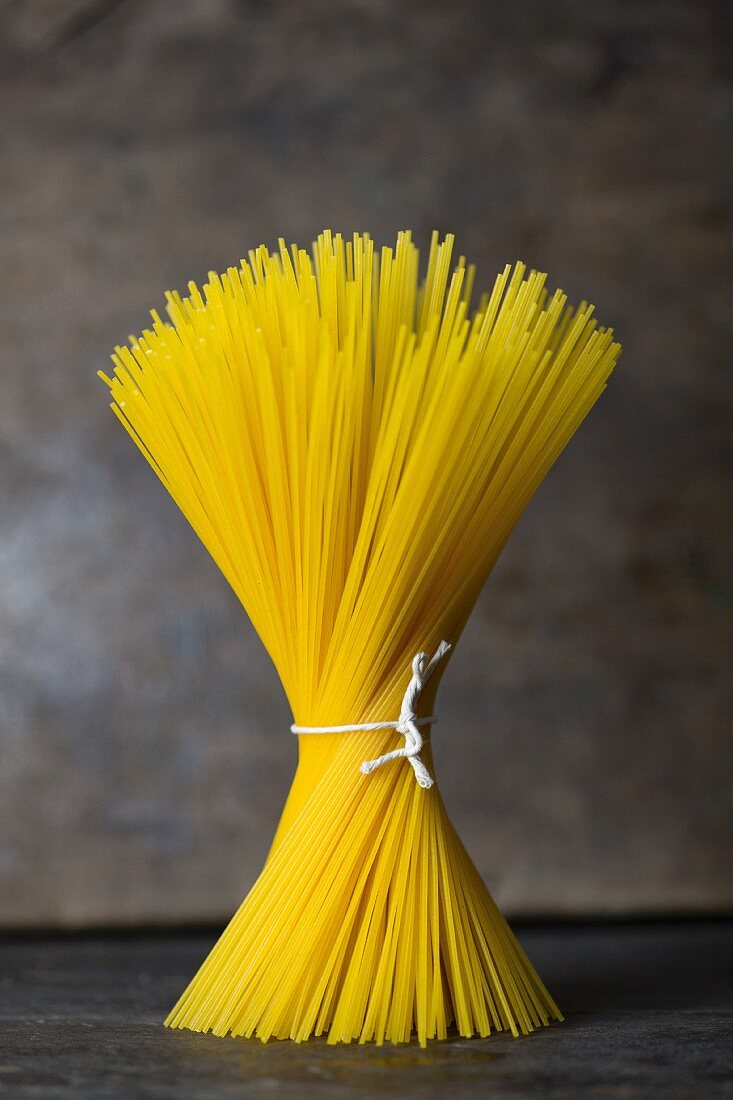 A bundle of spaghetti tied with string standing on a grey surface