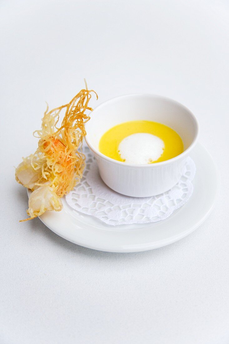 Cream of yellow pepper soup with a crispy prawn on a rice leaf