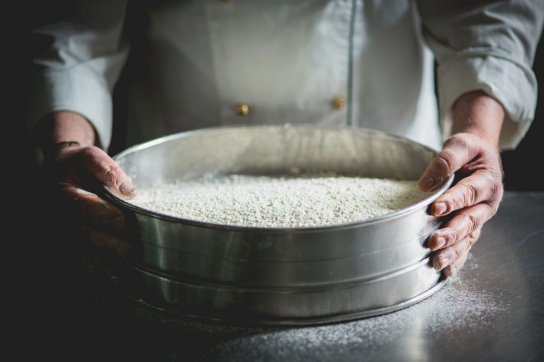 A confectioner with a large sieve of icing sugar