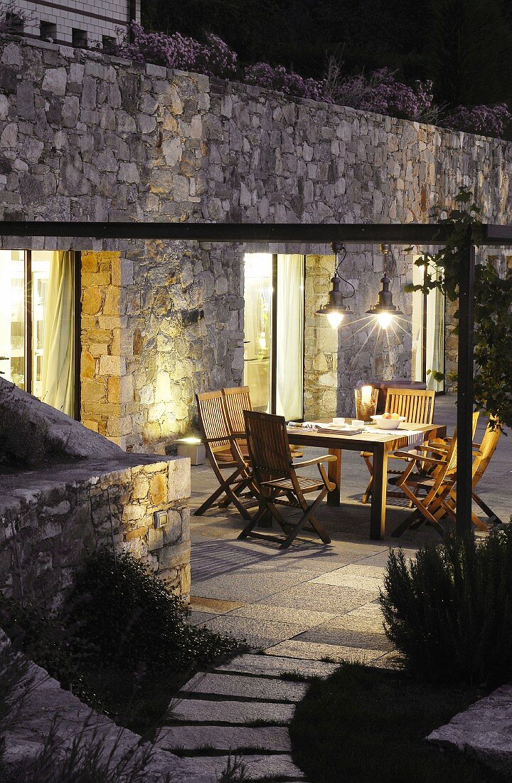 Garden furniture on illuminated terrace against stone façade