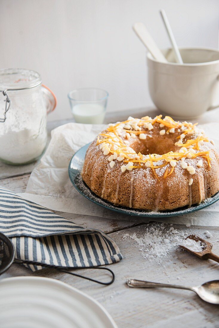A white chocolate Bundt cake with orange zest on a table with baking utensils