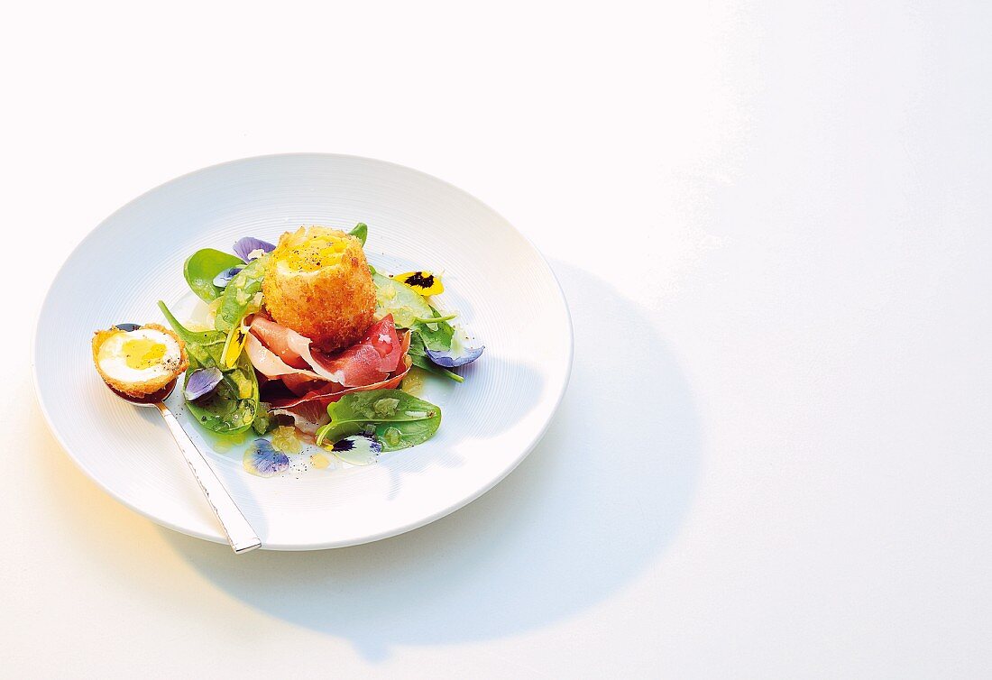 A baked egg wrapped in Parmesan cheese and ham on a salad of edible flowers
