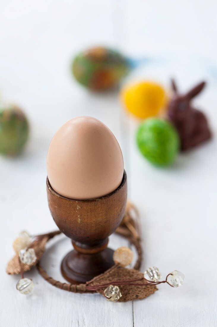 Close up von einem Ei im Eierbecher vor bunten Eiern und Osterhasen im Hintergrund