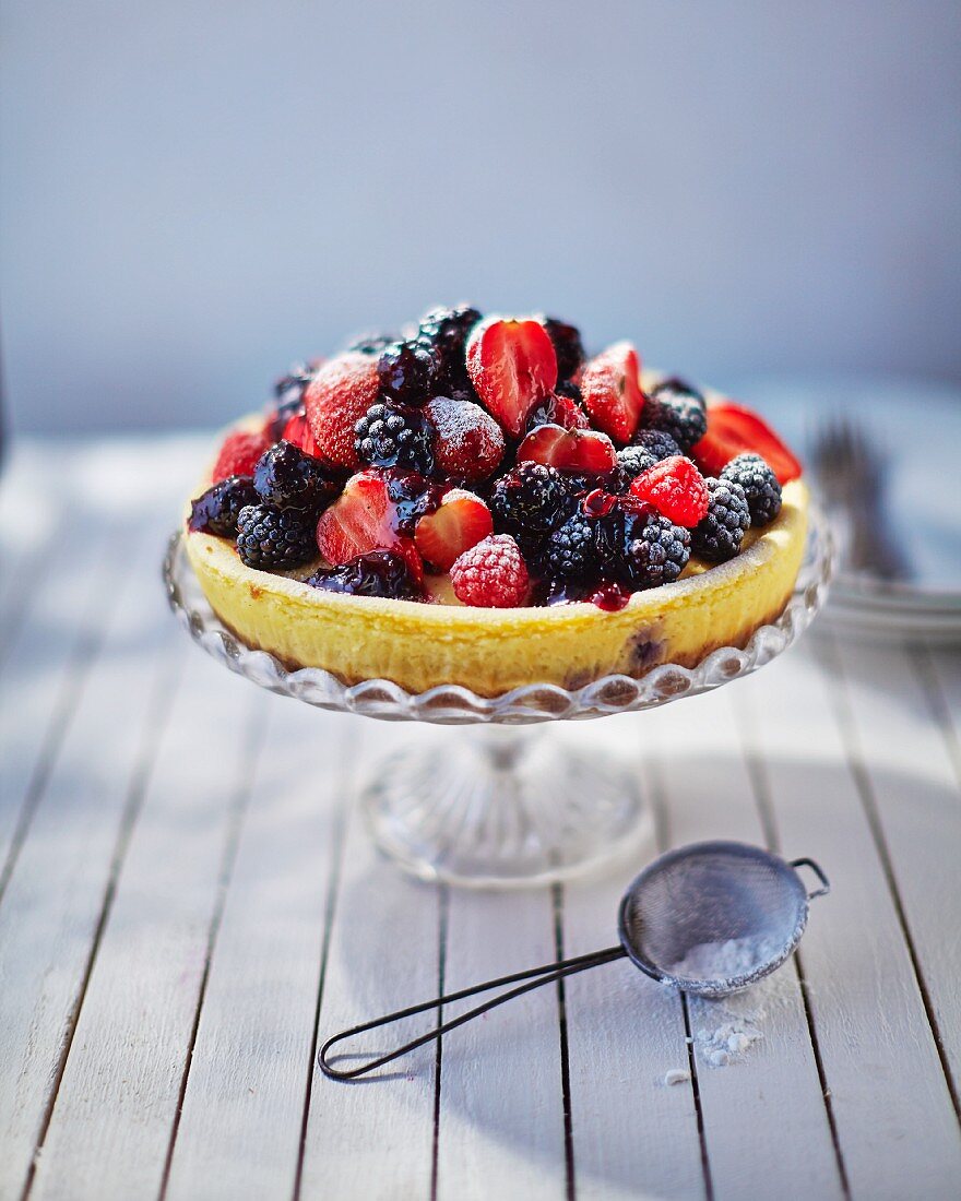 A mixed berry tart dusted with icing sugar on a cake stand