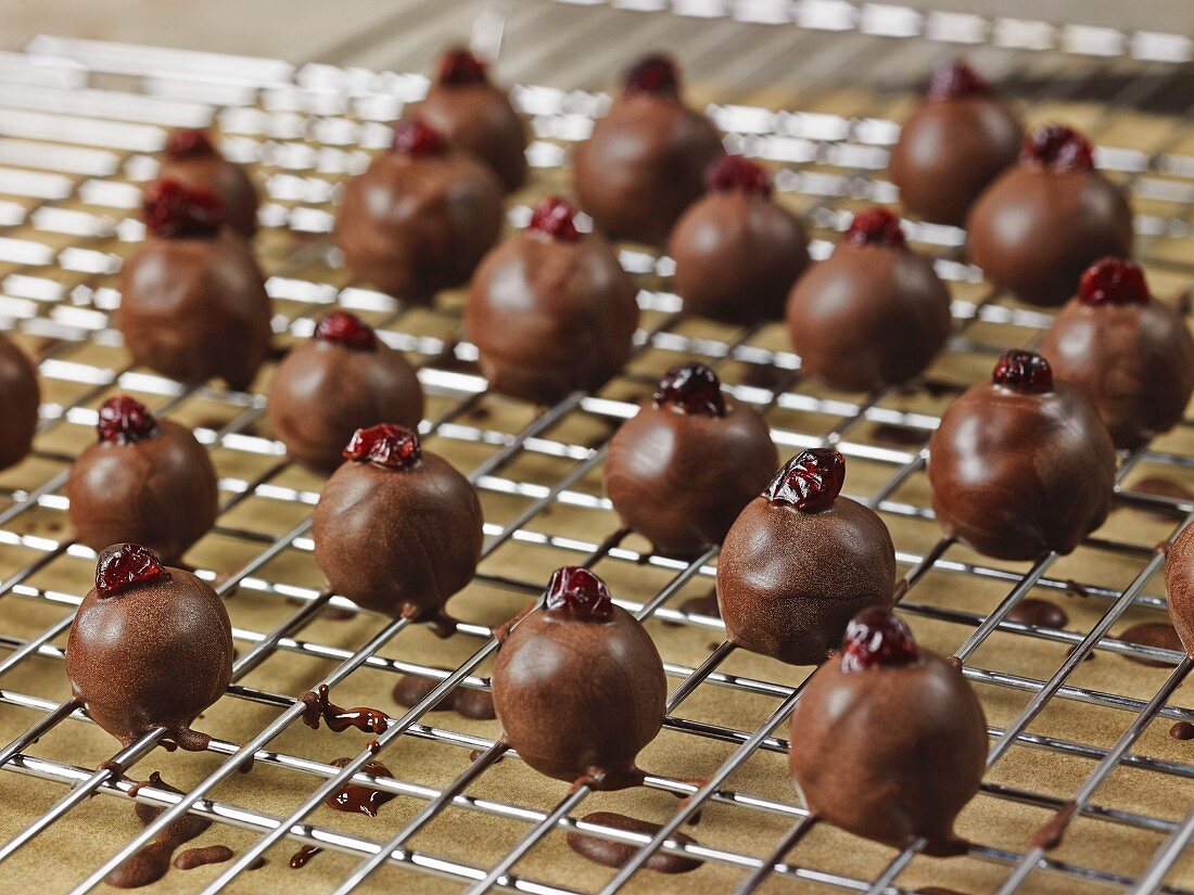 Dark chocolate coated, handrolled marzipan truffles with cranberries drying on a wire rack