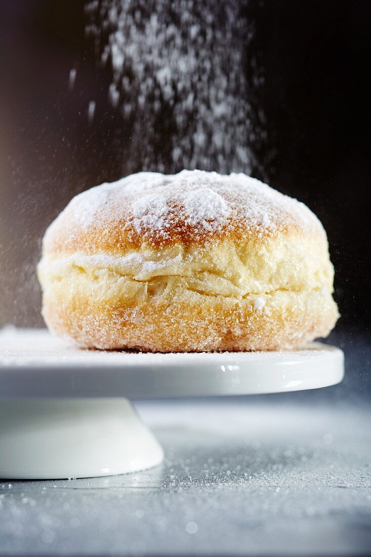 A doughnut being dusted with icing sugar (close-up)