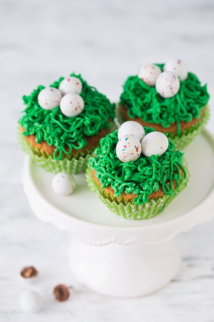 Oster-Cupcakes mit grüner Buttercreme und Zuckereiern auf Kuchenständer