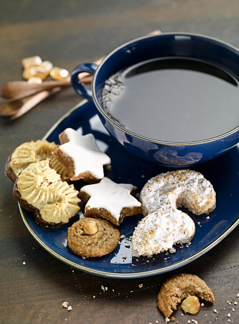 Various Christmas biscuits on a plate with a cup of tea