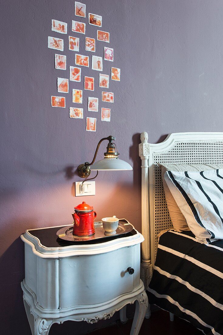 Antique bedside cabinet and vintage sconce lamp below arrangement of photos on mauve wall in bedroom