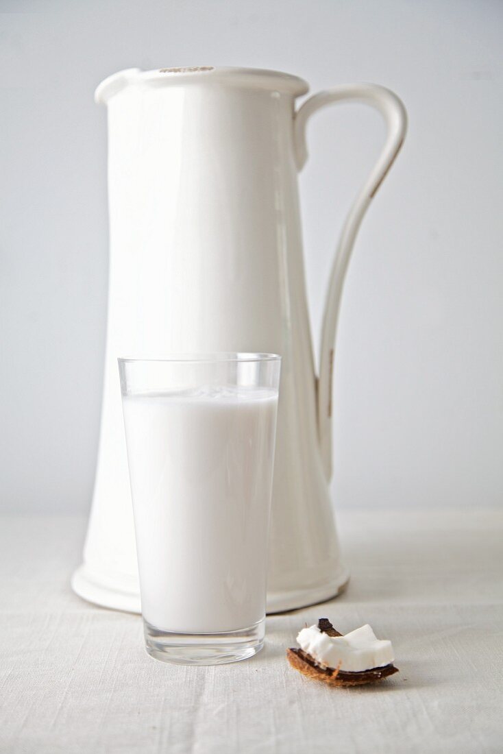 Coconut milk in a glass with a white jug behind it