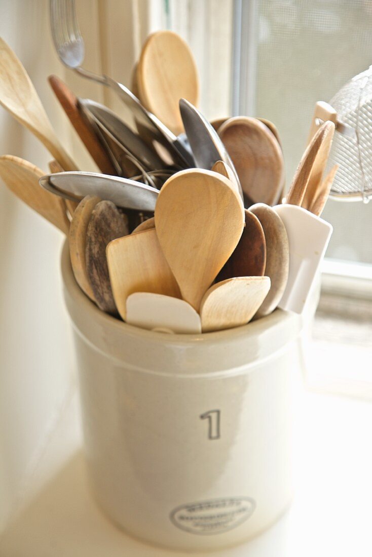 Wooden and metal spoons in a ceramic pot on a kitchen window sill
