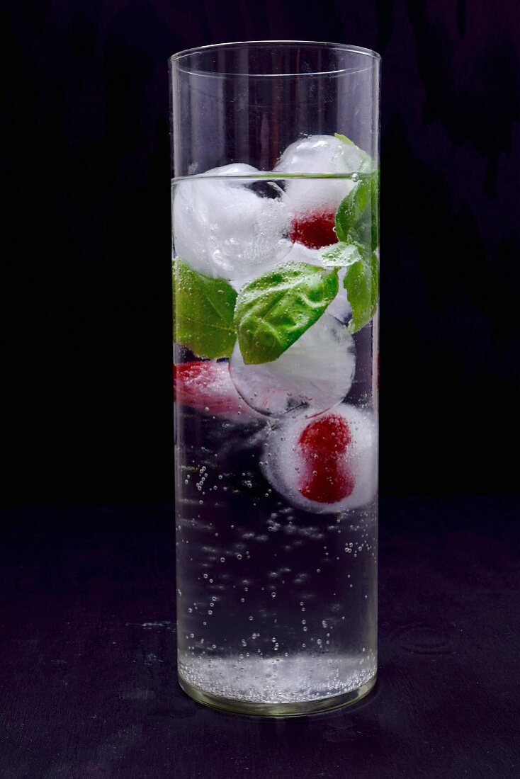 Ice cubes with raspberries and basil in a glass of water