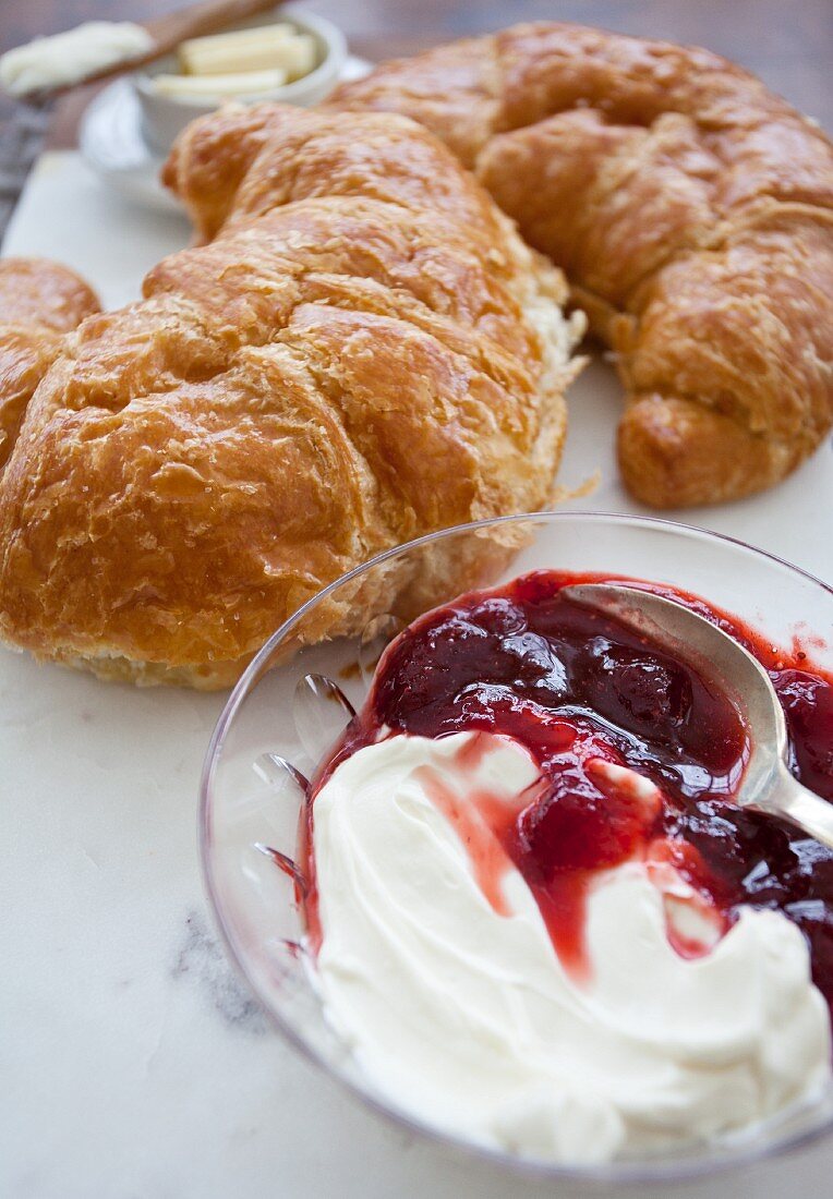 Strawberry jam and cream cheese in a glass bowl in front of two croissants