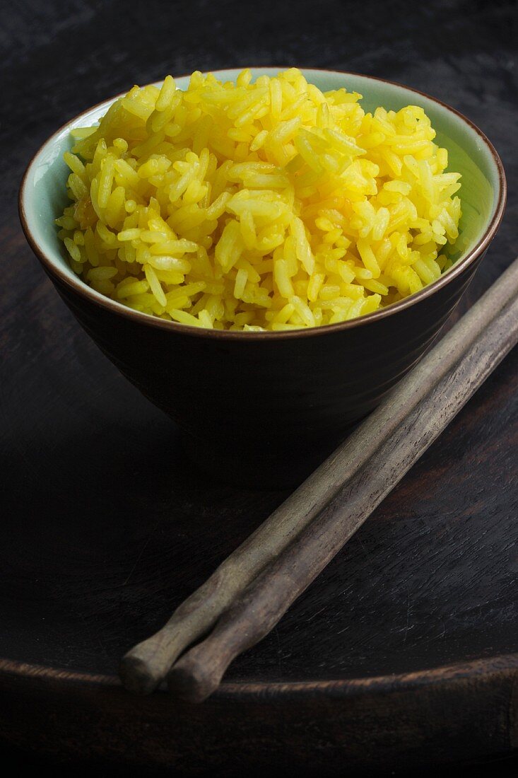 A bowl of saffron rice with chopsticks on a black wooden plate