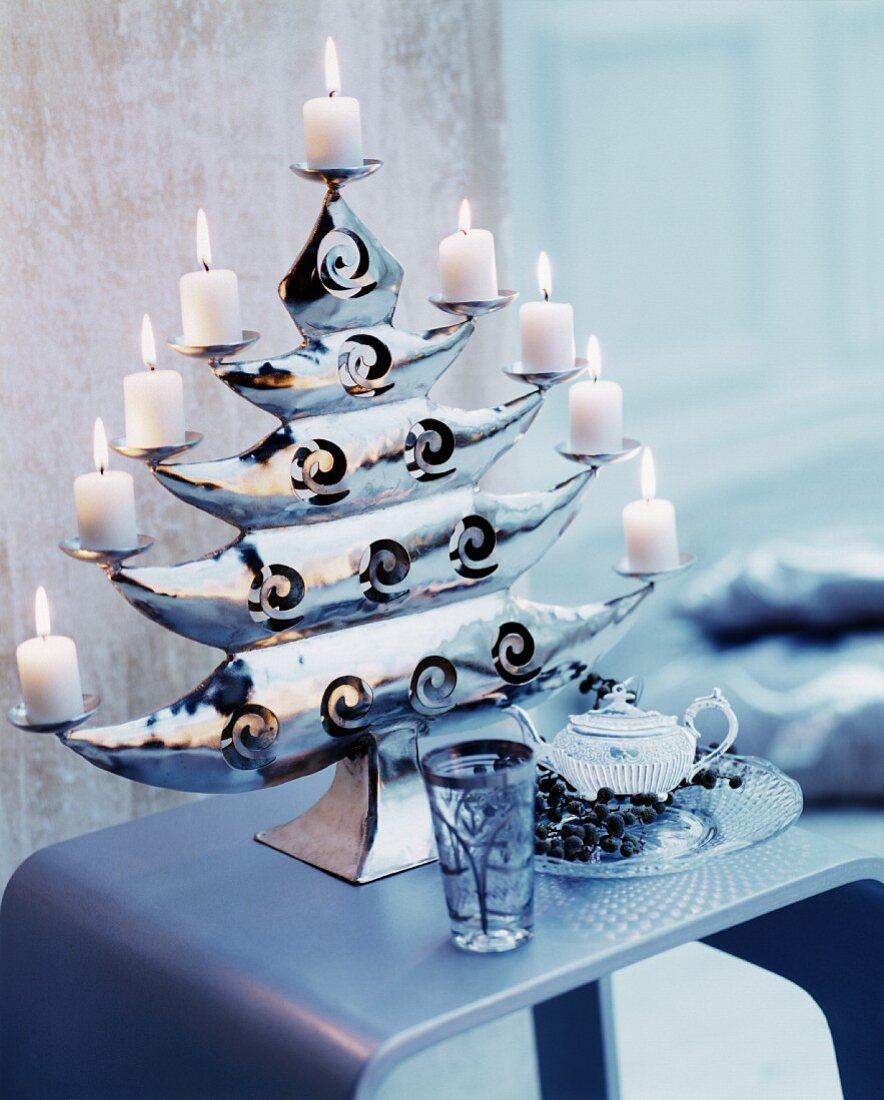 Eleganter glänzender Kerzenständer in Baumform mit brennenden weißen Stumpenkerzen