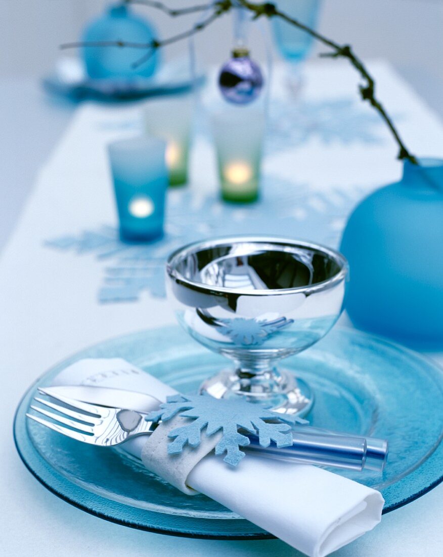Festliches Gedeck mit eisblauen Glastellern und glänzendem Kelch, dekoriert mit Serviettenring aus Filz