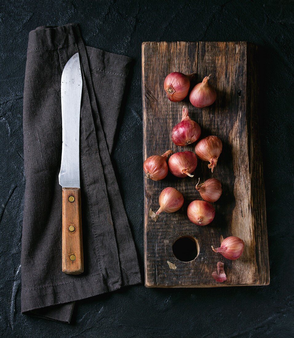 Small red onions on a wooden board and an old knife on a fabric napkin
