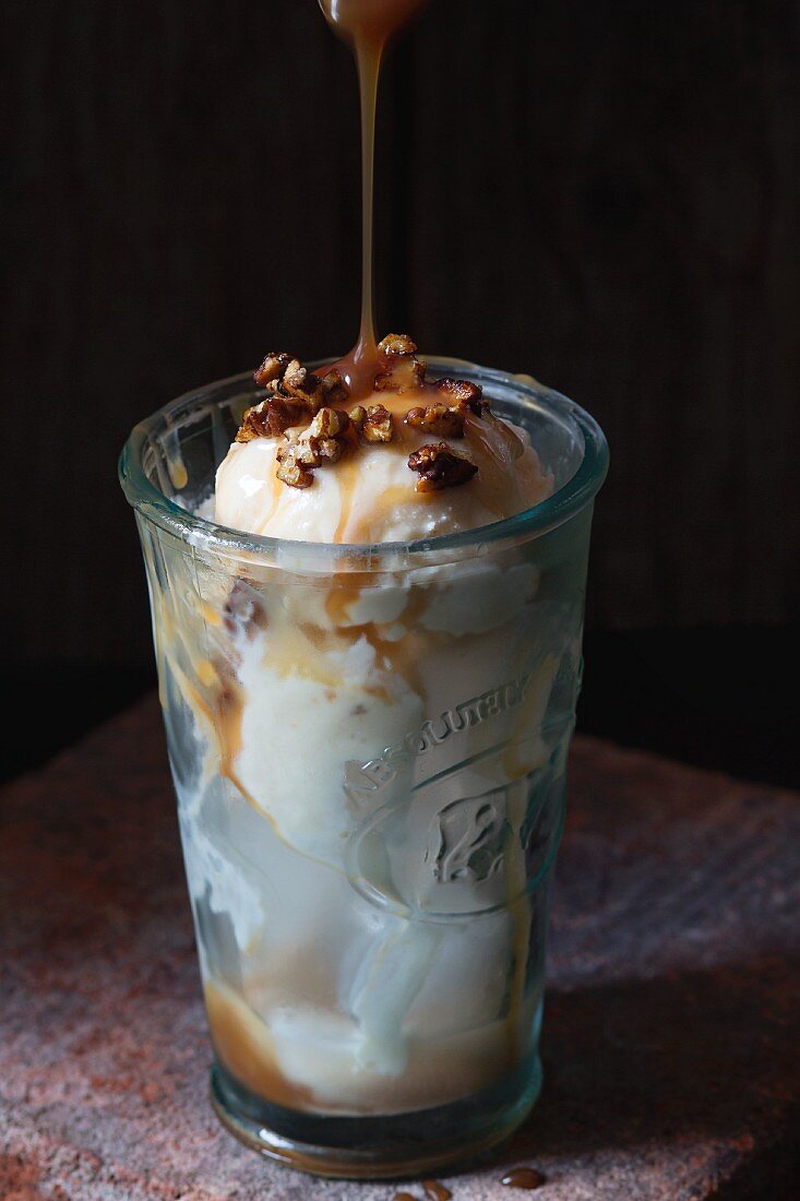 Caramel and hazelnut butter ice cream with caramel sauce and crispy nuts in a glass with ice cubes