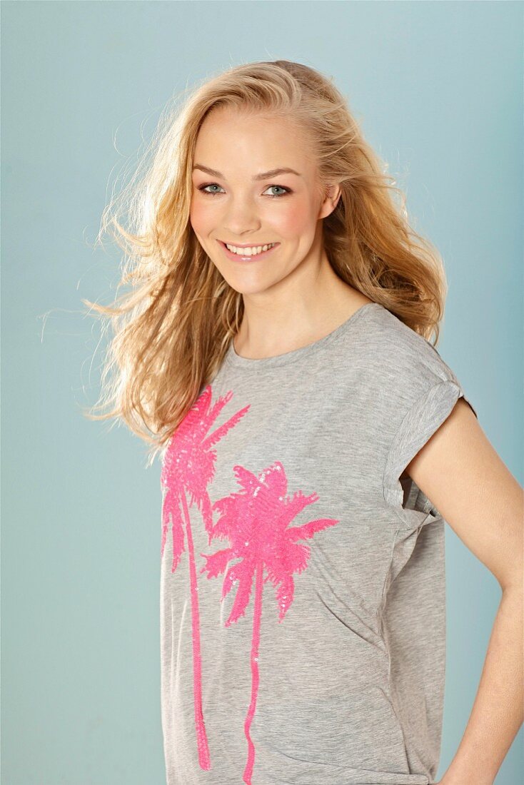 A young blonde woman wearing a grey sequinned T-shirt with palm trees