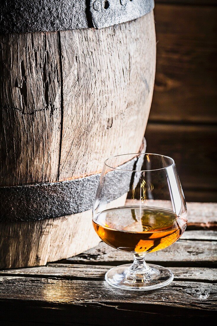 Glas Cognac neben altem Holzfass