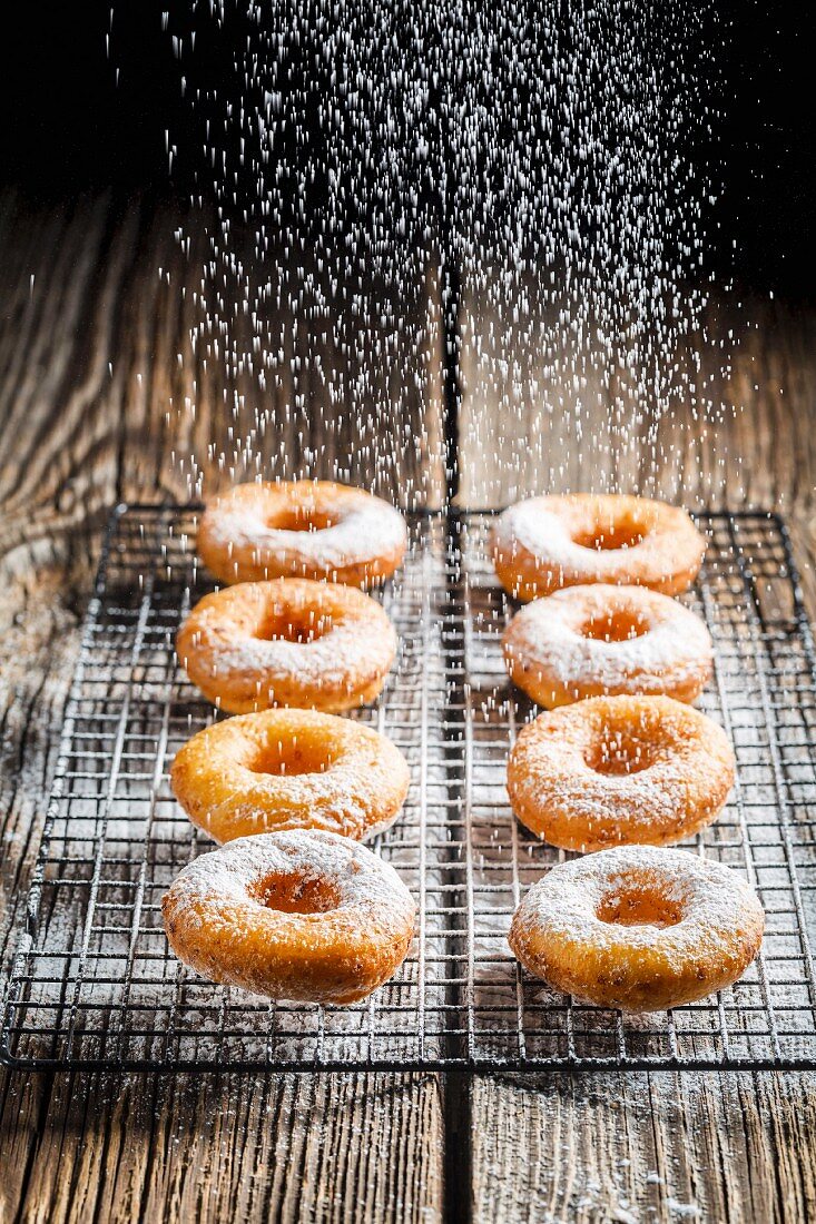 Freshly baked doughnuts being dusted with icing sugar