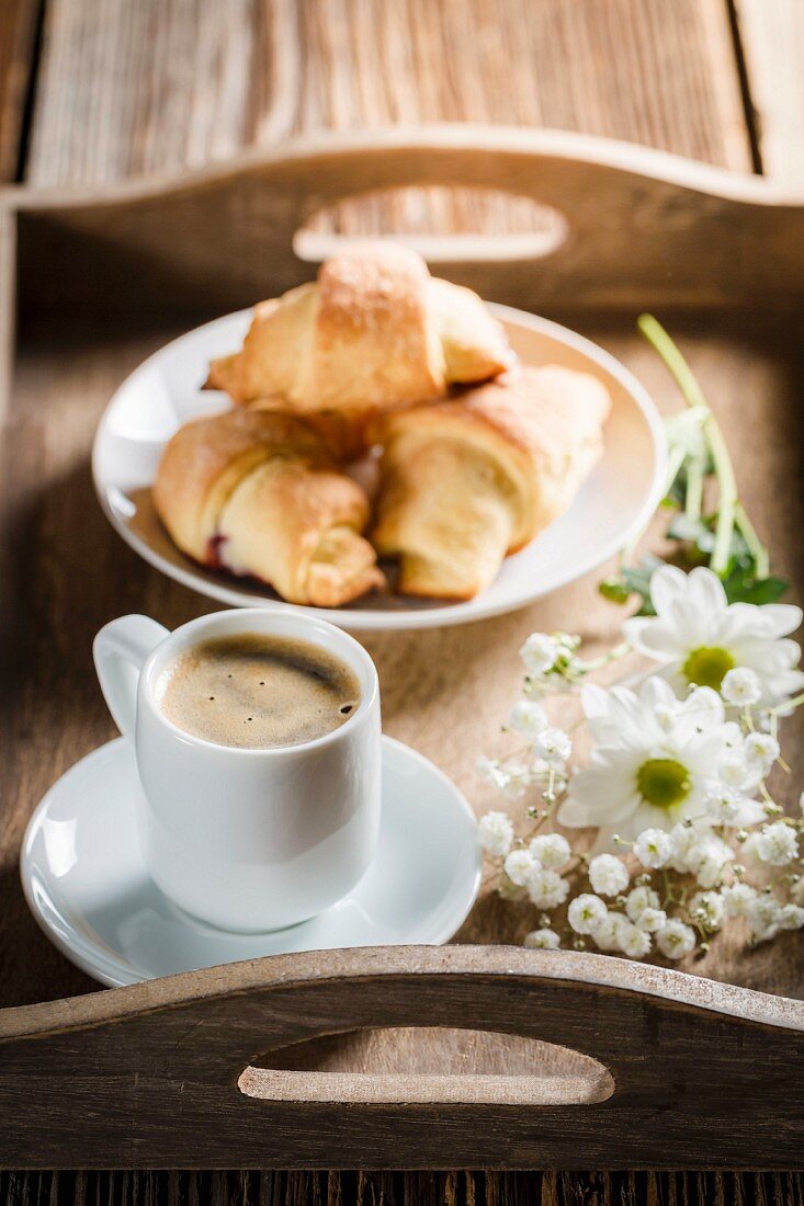 Espresso, Croissants und Blumen auf Holztablett